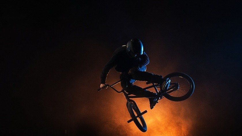 Rider de BMX en el aire de noche en un skatepark, iluminado por una luz naranja